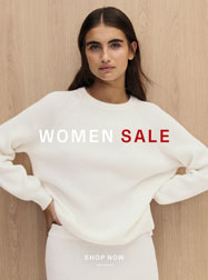 WOMEN SALE: Frau im hellen Stricklook vor Holzfläche, mit rotem ‚SALE‘ Schriftzug präsentiert – reduzierte Premium‑Damenmode.