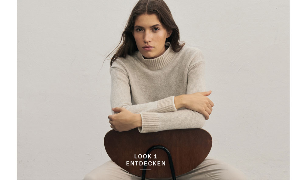 Favourite New Look Frau sitzt lässig auf dem Stuhl und trägt einen Rollkragenpullover aus 100% Schurwolle in Creme.