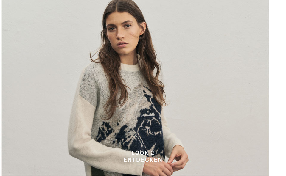 Favourite New Look Eine Frau blickt in die Kamera und trägt einen weichen Pullover mit einem Bergmotiv in Pastelltönen.