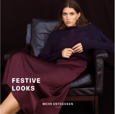 Festive Looks Frau sitzt im Ledersessel, trägt dunkelblauen Alpaka-Mix-Pullover und langen bordeauxroten Rock – Festive Look.