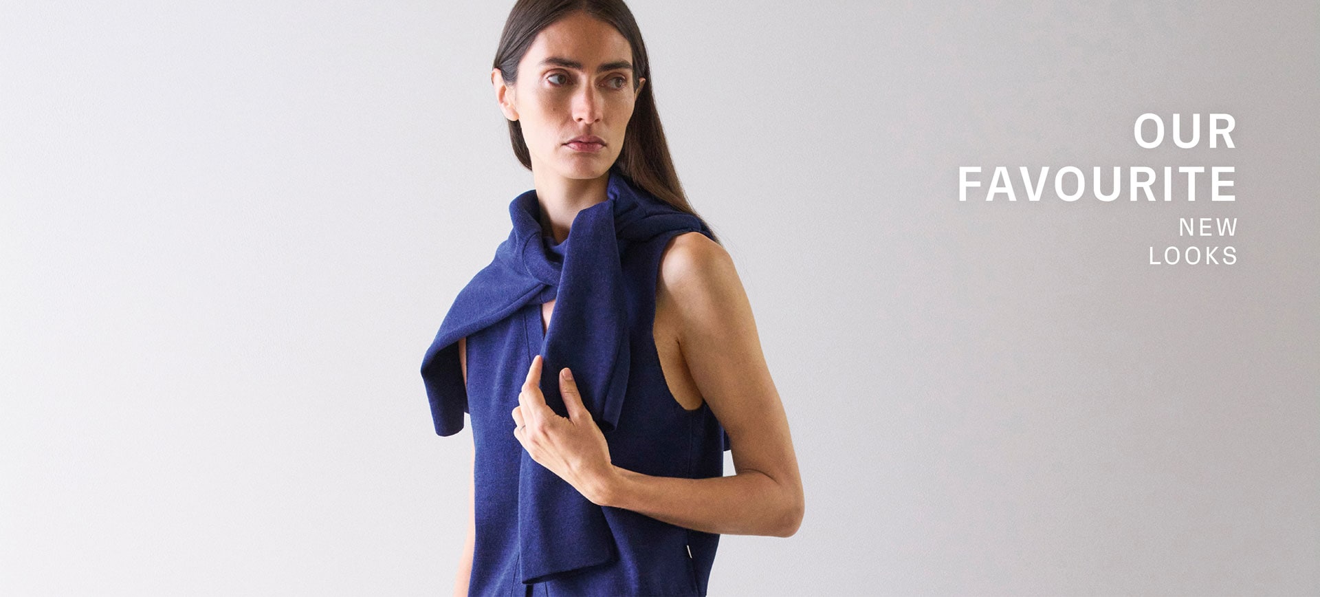 Our Favourite New Looks: Frau in modernem Navy Stricklook mit locker übergeworfenem Pullover, clean inszeniert vor ruhigem Hintergrund für eine zeitlose Premium Ästhetik.