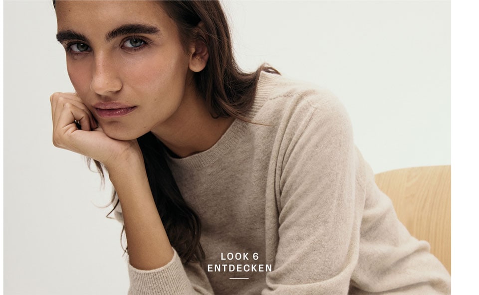 Look 6 entdecken: Frau in weichem Feinstrick Pullover in warmem Beige, minimalistisch inszeniert für eine natürliche, hochwertige Premium Note.