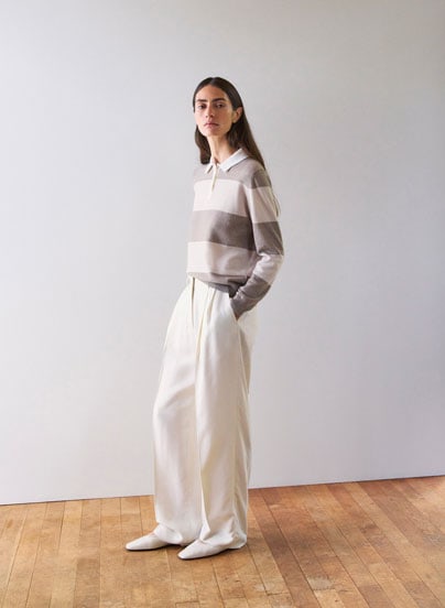 Frau im gestreiften Strick Polo in soften Naturtönen und weiter Hose, modern und ruhig inszeniert für eine edle Premium Ästhetik.