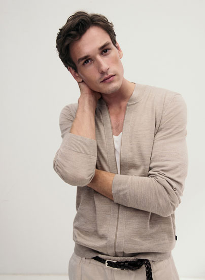 Mann in leichter Strickjacke und weißem Shirt, modern und entspannt inszeniert für eine natürliche, hochwertige Premium Ästhetik.