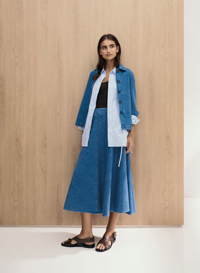 Frau im modernen Knitted Denim Set aus Jacke, Hemd und Rock – strukturierter Baumwollstrick für zeitlose Premium Eleganz.