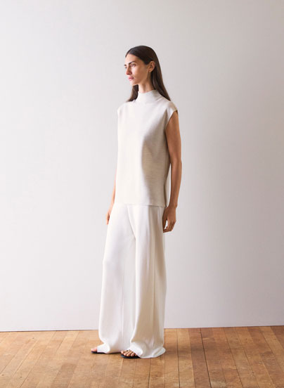 Frau in hellem Stricktop und weiter Hose, minimalistisch im Studio inszeniert – hochwertige Knitwear für moderne Premium Looks.
