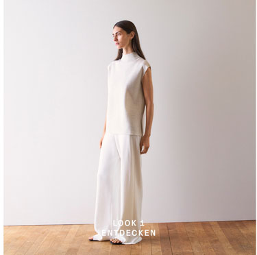 Look 1 entdecken: Frau in hellem Stricktop und weiter Hose, minimalistisch im Studio inszeniert – hochwertige Knitwear für moderne Premium Looks.