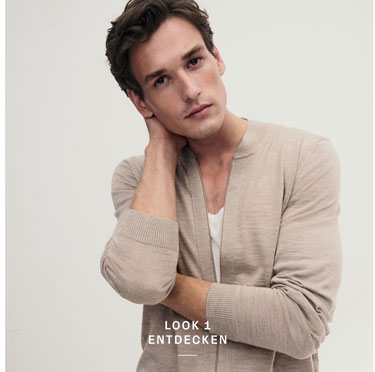 Look 1 entdecken: Mann in leichter Strickjacke und weißem Shirt, modern und entspannt inszeniert für eine natürliche, hochwertige Premium Ästhetik.