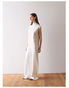 Frau in hellem Stricktop und weiter Hose, minimalistisch im Studio inszeniert – hochwertige Knitwear für moderne Premium Looks.