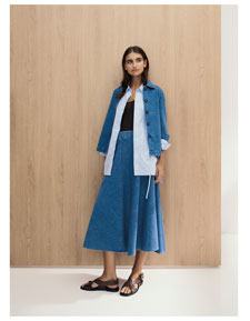 Frau im modernen Knitted Denim Set aus Jacke, Hemd und Rock – strukturierter Baumwollstrick für zeitlose Premium Eleganz.