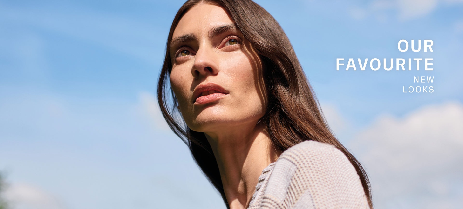 Our Favourite New Look: Frau in heller Strickjacke mit grafischem Muster, ruhig vor blauem Himmel inszeniert.