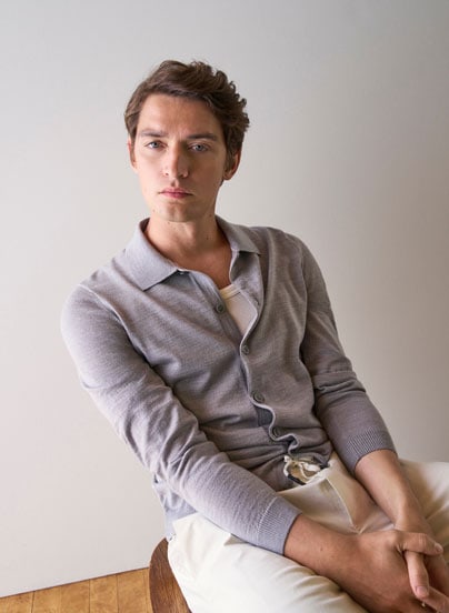 Our Favourite New Looks: Mann in feiner Strickjacke und heller Hosen, lässig im modernen Indoor Setting präsentiert.