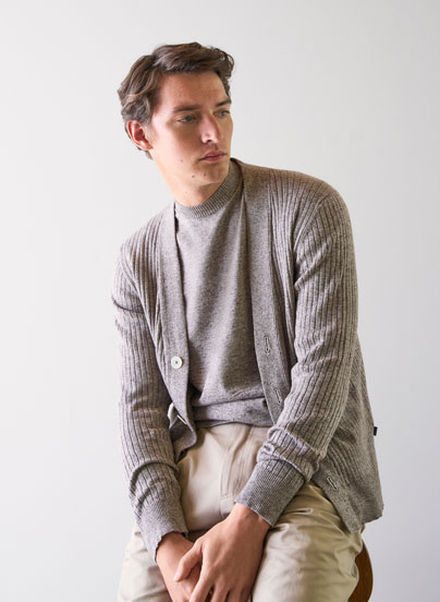 Our Favourite New Looks: Mann in feiner Strickjacke und heller Hosen, lässig im modernen Indoor Setting präsentiert.