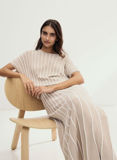 Our Favourite New Looks: Frau im gestreiftem Strickoberteil mit passendem Rock, klar und modern auf hellem Stuhl vor minimalistischem Hintergrund inszeniert.