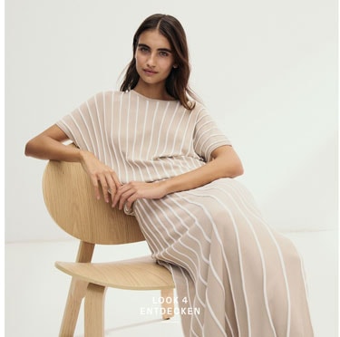 Look 4 entdecken: Our Favourite New Looks. Frau im gestreiftem Strickoberteil mit passendem Rock, klar und modern auf hellem Stuhl vor minimalistischem Hintergrund inszeniert.