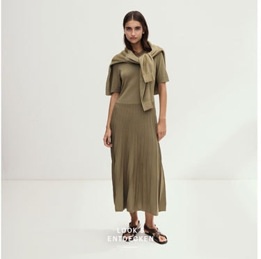 Look 5 entdecken: Our Favourite New Looks. Frau in olivfarbenem Kleid und umgelegter Strickjacke, minimalistisch im Studio inszeniert.