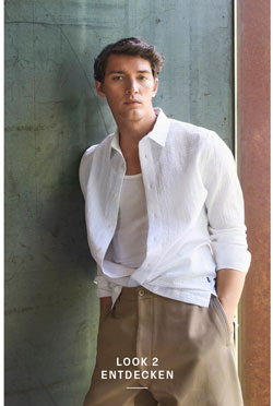 Look 2 entdecken: Our Favourite New Looks. Mann in lässigem weißen Hemd und hellen Hosen, entspannt an Wandfläche präsentiert – ein moderner, reduzierter Premium Casual Style.