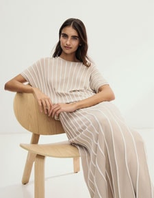 Our Favourite New Looks: Frau im gestreiftem Strickoberteil mit passendem Rock, klar und modern auf hellem Stuhl vor minimalistischem Hintergrund inszeniert.