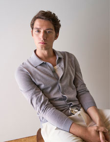 Our Favourite New Looks: Mann in feiner Strickjacke und heller Hosen, lässig im modernen Indoor Setting präsentiert.