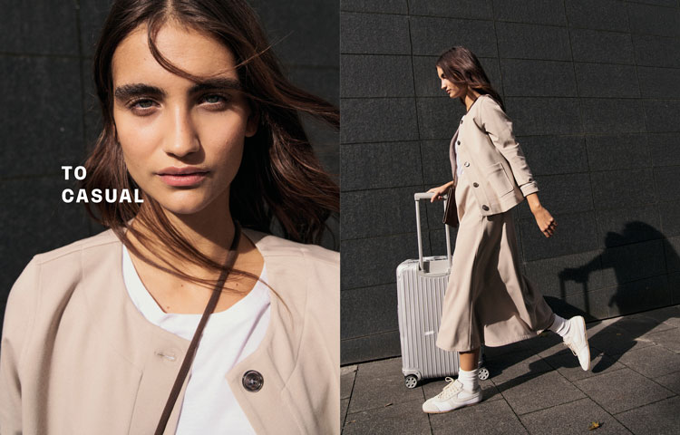 Frau in hellem TO CASUAL Look mit Jacke, Shirt und Rock, dynamisch mit Trolley unterwegs – modern urban inszeniert.