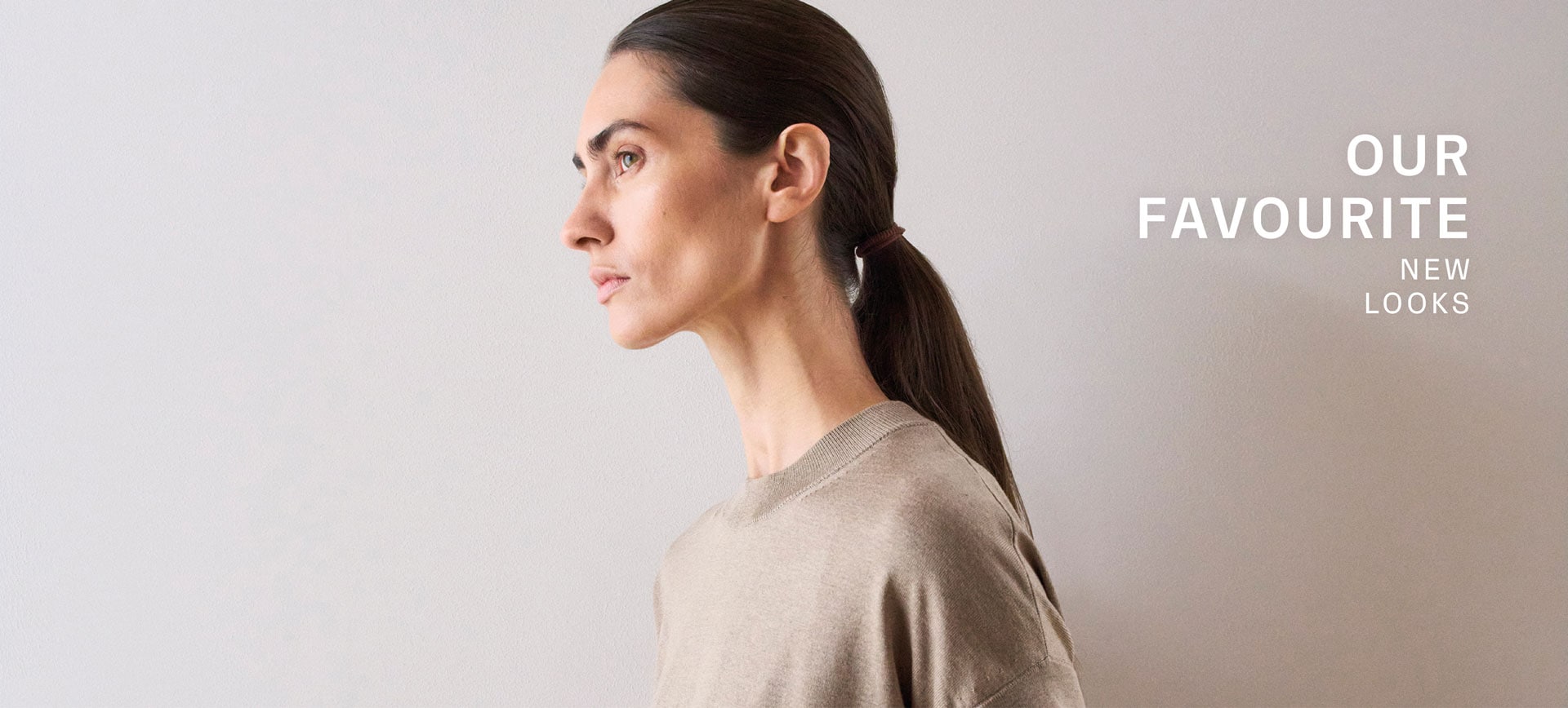Our Favourite New Looks: Frau im soften, beigefarbenen Stricktop, seitlich vor heller Wand inszeniert – moderner, reduzierter Spring‑Summer Look.