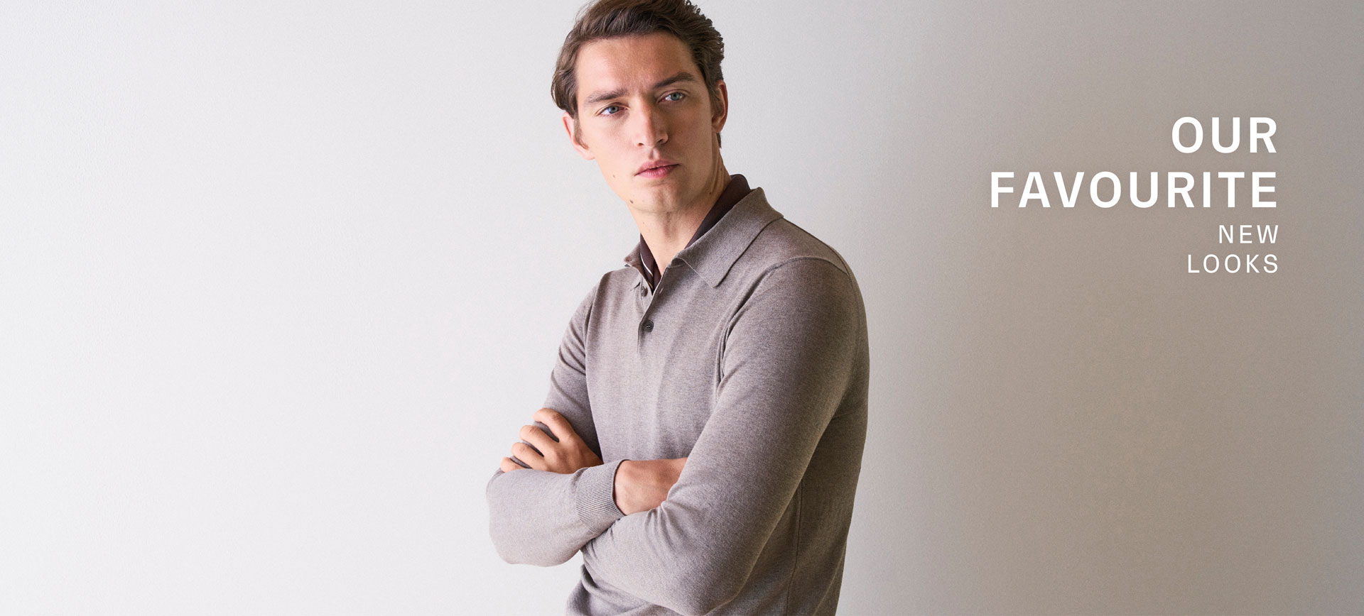 Our Favourite New Looks: Mann im feinen, beigefarbenen Strickpolo, seitlich vor heller Wand inszeniert – moderner, reduzierter Spring‑Summer Look.