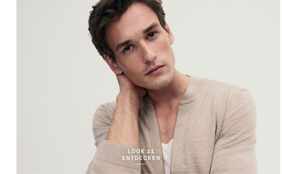 Look 11 entdecken: Our Favourite New Looks. Mann in leichter Strickjacke und weißem Shirt, modern und entspannt inszeniert für eine natürliche, hochwertige Premium Ästhetik.