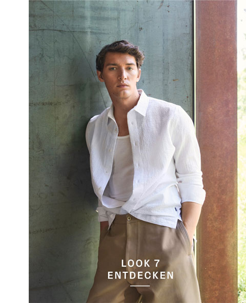 Look 7 entdecken: Our Favourite New Looks. Mann in lässigem weißen Hemd und hellen Hosen, entspannt an Wandfläche präsentiert – ein moderner, reduzierter Premium Casual Style.