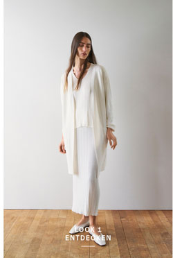 Look 1 entdecken: Our Favourite New Looks: Frau in langem, cremefarbenem Strick Ensemble mit offenem Cardigan, ruhig im Studio vor heller Wand inszeniert, leichte Premium Strickqualität.