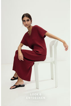 Look 6 entdecken: Our Favourite New Looks: Frau im bordeauxfarbenen Strickensemble, modern auf hellem Stuhl im Studio inszeniert.