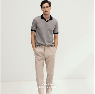 Look 10 entdecken: Our Favourite New Looks. Mann im modernen Strickpolo mit dunklem Kragen und heller Hose, clean im Studio präsentiert – ein smarter Premium Everyday Look.