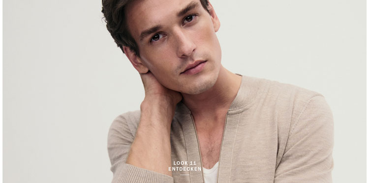 Look 11 entdecken: Our Favourite New Looks. Mann in leichter Strickjacke und weißem Shirt, modern und entspannt inszeniert für eine natürliche, hochwertige Premium Ästhetik.