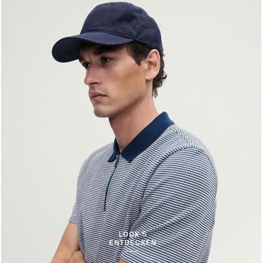 Look 5 entdecken: Our Favourite New Looks: Mann im fein gemusterten Poloshirt und navyfarbener Cap, modern und reduziert im Studio inszeniert.
