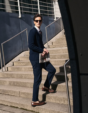 Monday to Friday: Mann im navyfarbenen Anzug mit Sonnenbrille und Tasche, klar auf Treppe im urbanen Umfeld inszeniert.