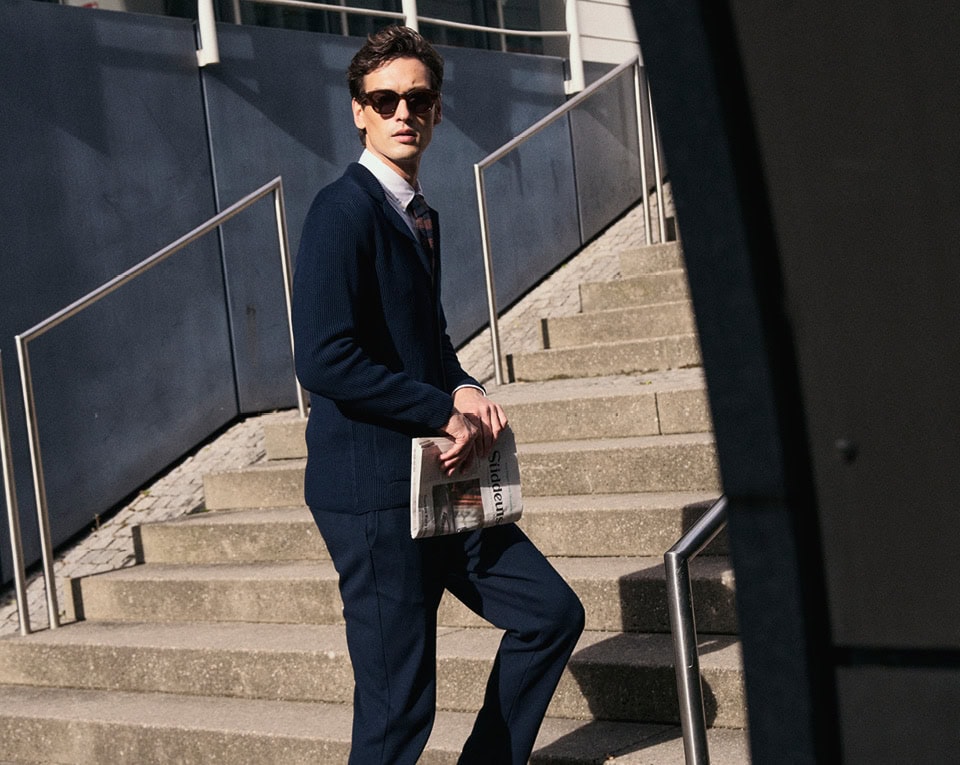 Monday to Friday: Mann im navyfarbenen Anzug mit Sonnenbrille und Tasche, klar auf Treppe im urbanen Umfeld inszeniert.