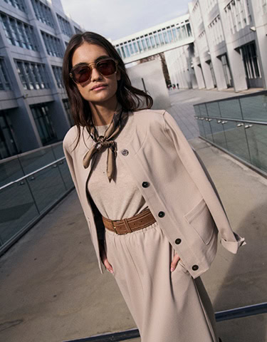 Monday to Friday: Frau im hellen Layer‑Look mit Blazer, Gürtel und Sonnenbrille, modern im urbanen Außenraum inszeniert.