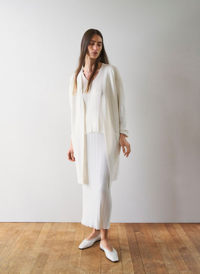 Look 1 entdecken: Our Favourite New Looks: Frau in langem, cremefarbenem Strick Ensemble mit offenem Cardigan, ruhig im Studio vor heller Wand inszeniert, leichte Premium Strickqualität.