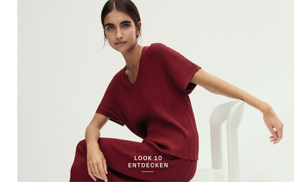 Look 10 entdecken: Our Favourite New Looks: Frau im bordeauxfarbenen Strickensemble, modern auf hellem Stuhl im Studio inszeniert.