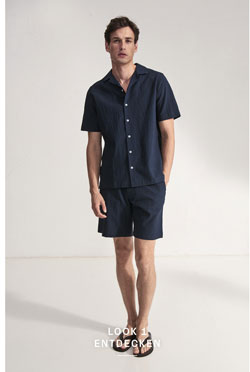 Look 1 entdecken: Our Favourite New Looks: Mann im navyfarbenen Sommer Set aus Kurzarmhemd und Shorts, clean im Studio inszeniert.