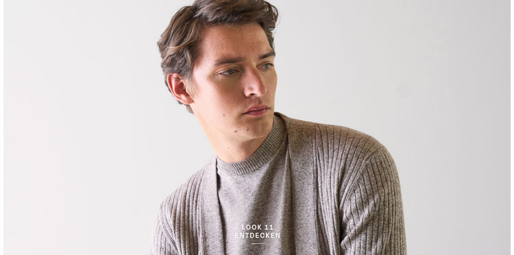 Look 11 entdecken: Our Favourite New Looks. Mann in feiner Strickjacke und heller Hosen, lässig im modernen Indoor Setting präsentiert.