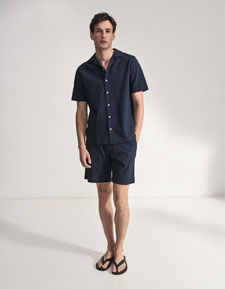 Our Favourite New Looks: Mann im navyfarbenen Sommer Set aus Kurzarmhemd und Shorts, clean im Studio präsentiert – lässiger Look zum Nachstylen.