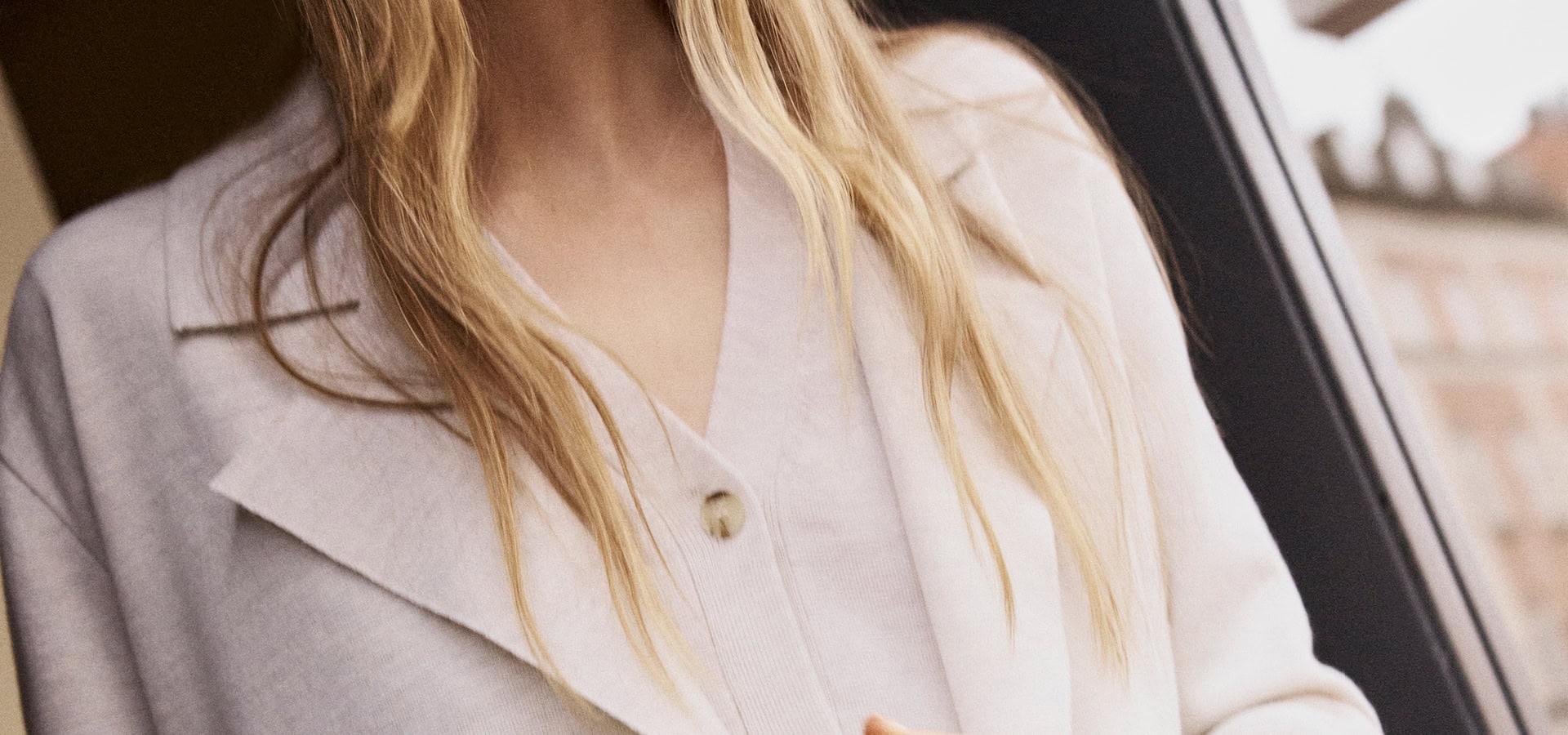 MONDAY TO FRIDAY Women: Frau im hellen Tailoring‑Look mit Blazer und Feinstrick, als Detailansicht vor urbanem Hintergrund präsentiert, moderne Premium‑Workwear.