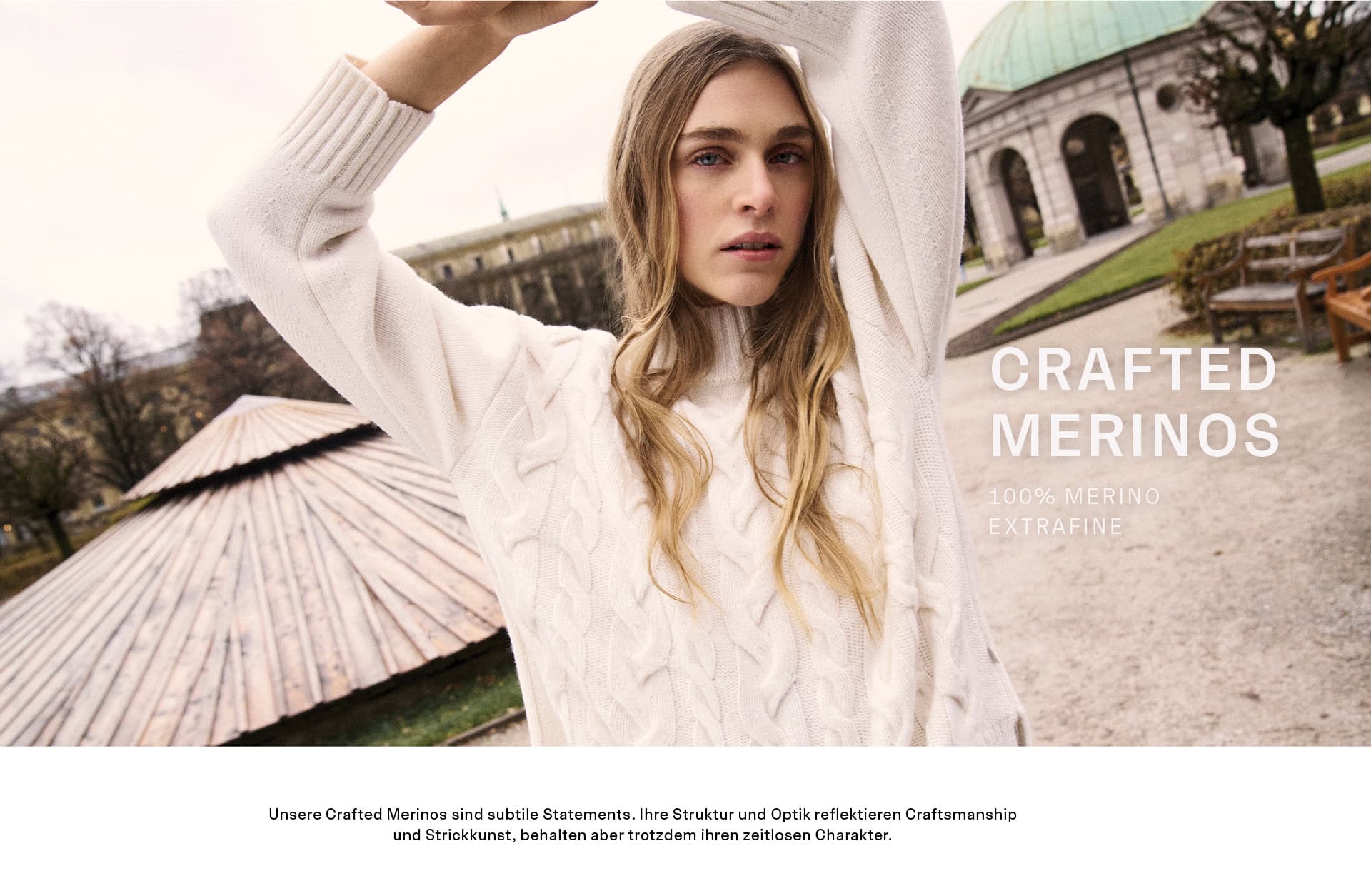 CRAFTED MERINOS CRAFTED MERINOS Women: Frau im hellen Zopfstrickpullover aus 100 % Merino extrafine vor historischer Architektur präsentiert. Strukturierte Merino‑Styles mit zeitloser Strickkunst und hochwertiger Verarbeitung.