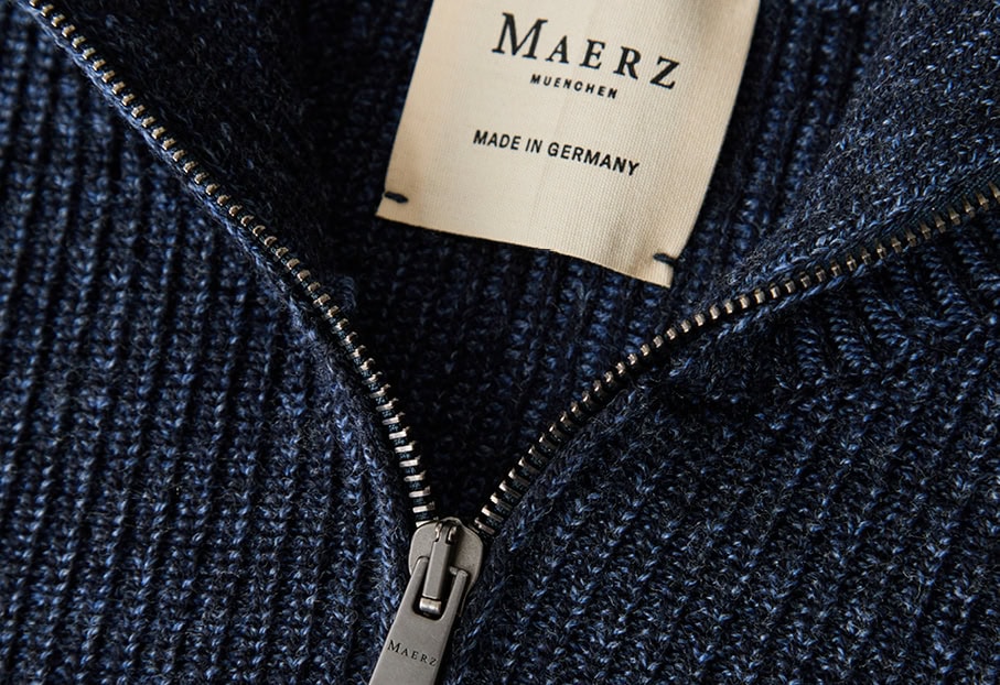MADE IN GERMANY: Detailansicht eines dunkelblauen Strickmodells mit Reißverschluss und Label, gefertigt aus 100 % Merino extrafine.