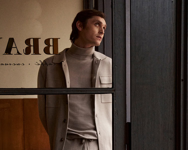 MONDAY TO FRIDAY Men: Mann im hellen Business‑Casual Look mit Rollkragen, modern im urbanen Café‑Setting inszeniert.