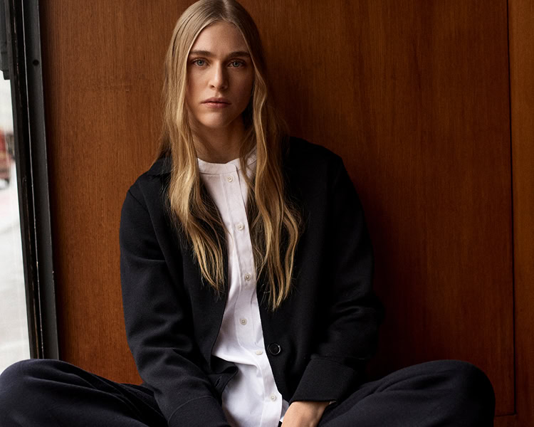 MONDAY TO FRIDAY Women: Frau im dunkelblauen Tailoring‑Look vor warmer Holzvertäfelung, moderne Premium‑Workwear.