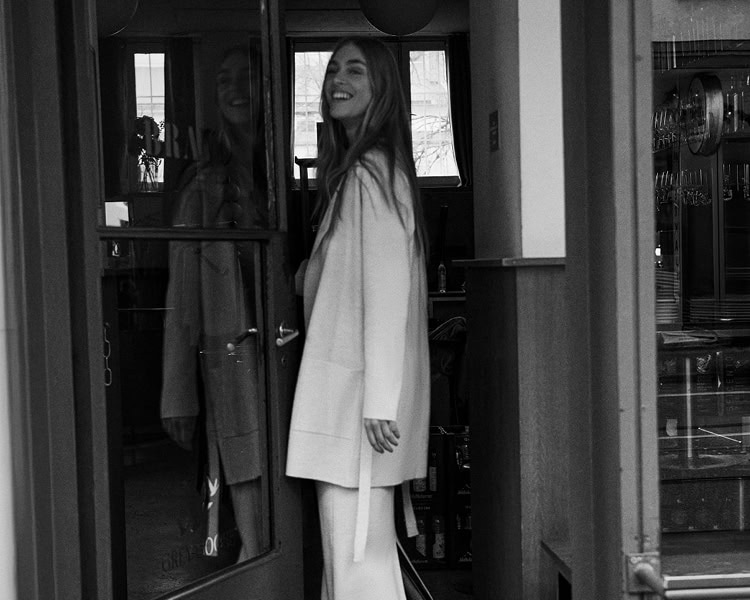 MONDAY TO FRIDAY: Frau im navyfarbenen Strick‑Blouson mit Reißverschluss, vor urbaner Architektur und Spiegelungen präsentiert, zeitlose Premium‑Workwear.