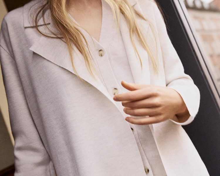MONDAY TO FRIDAY Women: Frau im hellen Tailoring‑Look mit Blazer und Feinstrick, als Detailansicht vor urbanem Hintergrund präsentiert, moderne Premium‑Workwear.