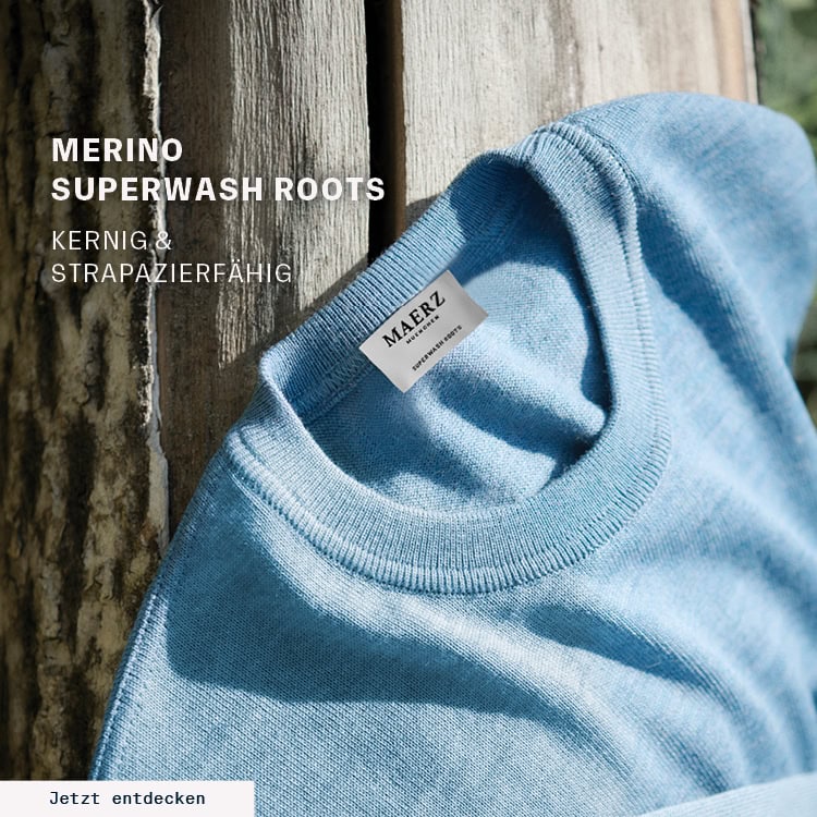MERINO SUPERWASH ROOTS: Hellblauer Merino‑Strick vor natürlicher Holzstruktur präsentiert, kernige und strapazierfähige Premium‑Qualität mit dem Call‑to‑Action ‚Jetzt entdecken‘.
