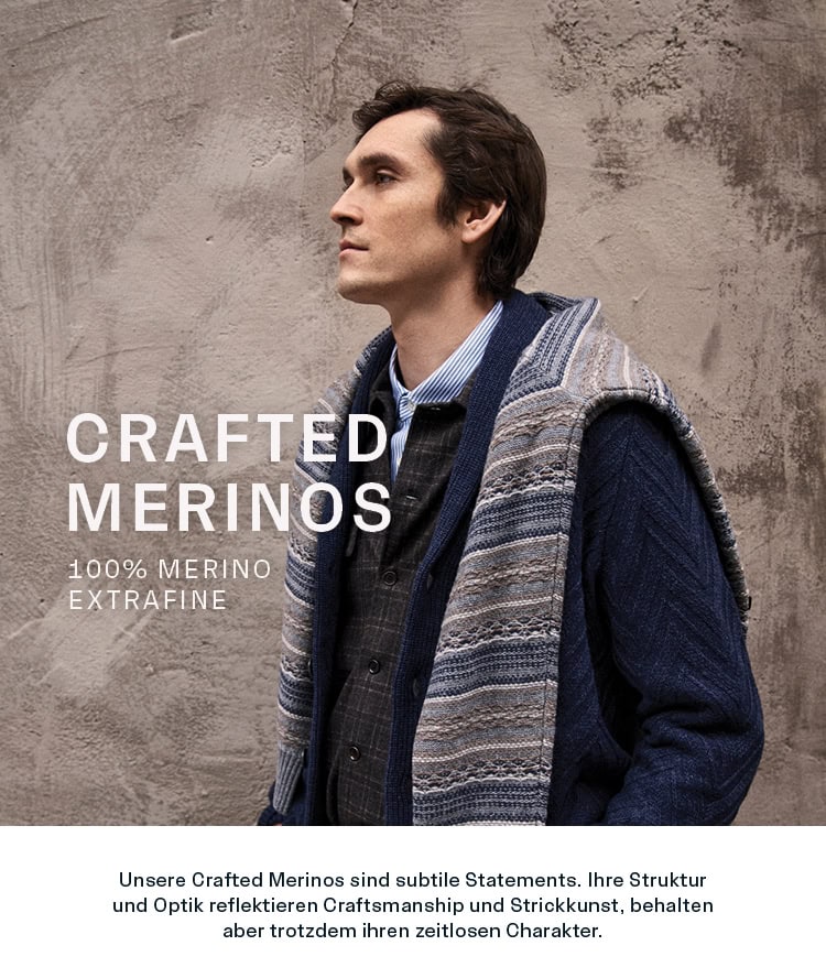CRAFTED MERINOS Men: Mann im Stricklook aus 100 % Merino extrafine mit Hemd und umgelegtem Pullover vor texturierter Wand präsentiert. Strukturierte Merino‑Styles mit zeitloser Strickkunst und hochwertiger Verarbeitung.
